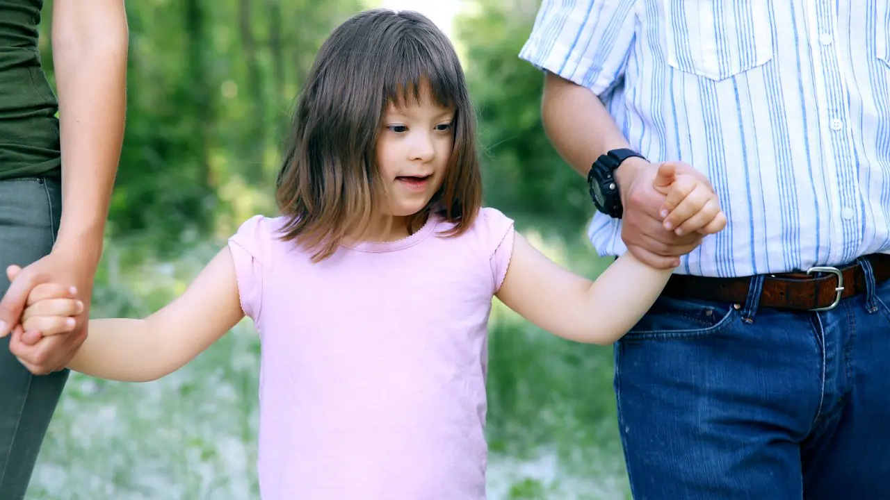 Young child with SEND walking holding hands with two adults.