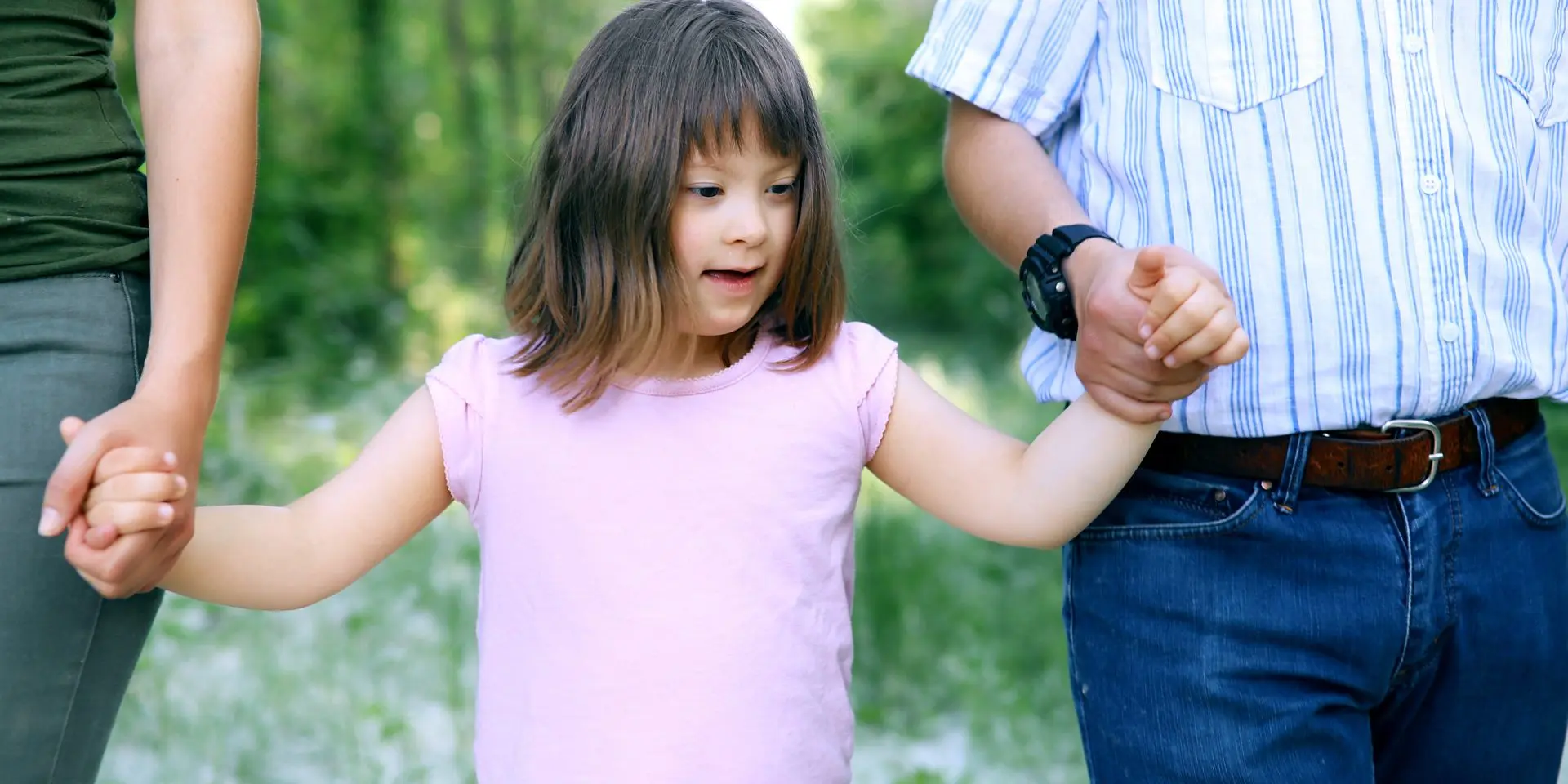 Young child with SEND walking holding hands with two adults.