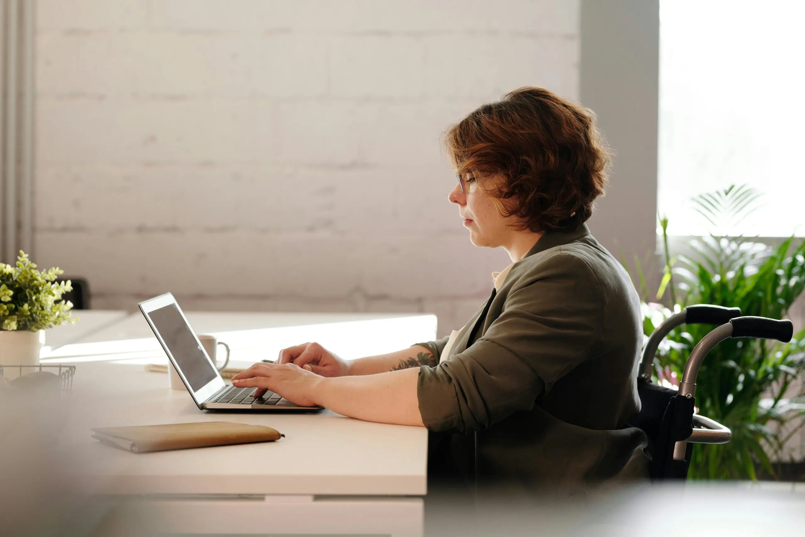 Woman who is a wheelchair user sitting at a desk typing on a laptop.