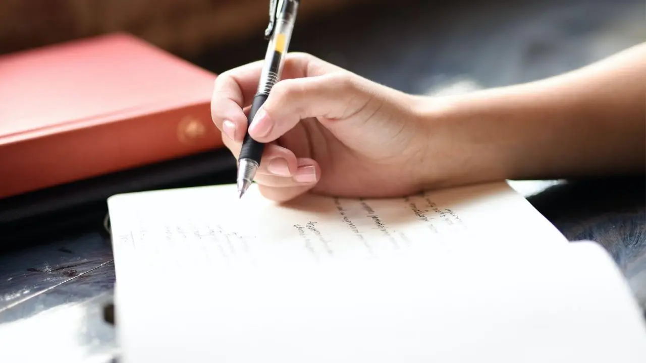 Open notepad with hand holding a pen and about to write