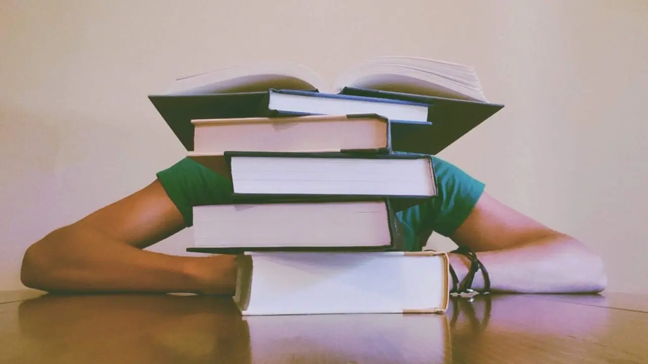 University student with head on hands behind a pile of books