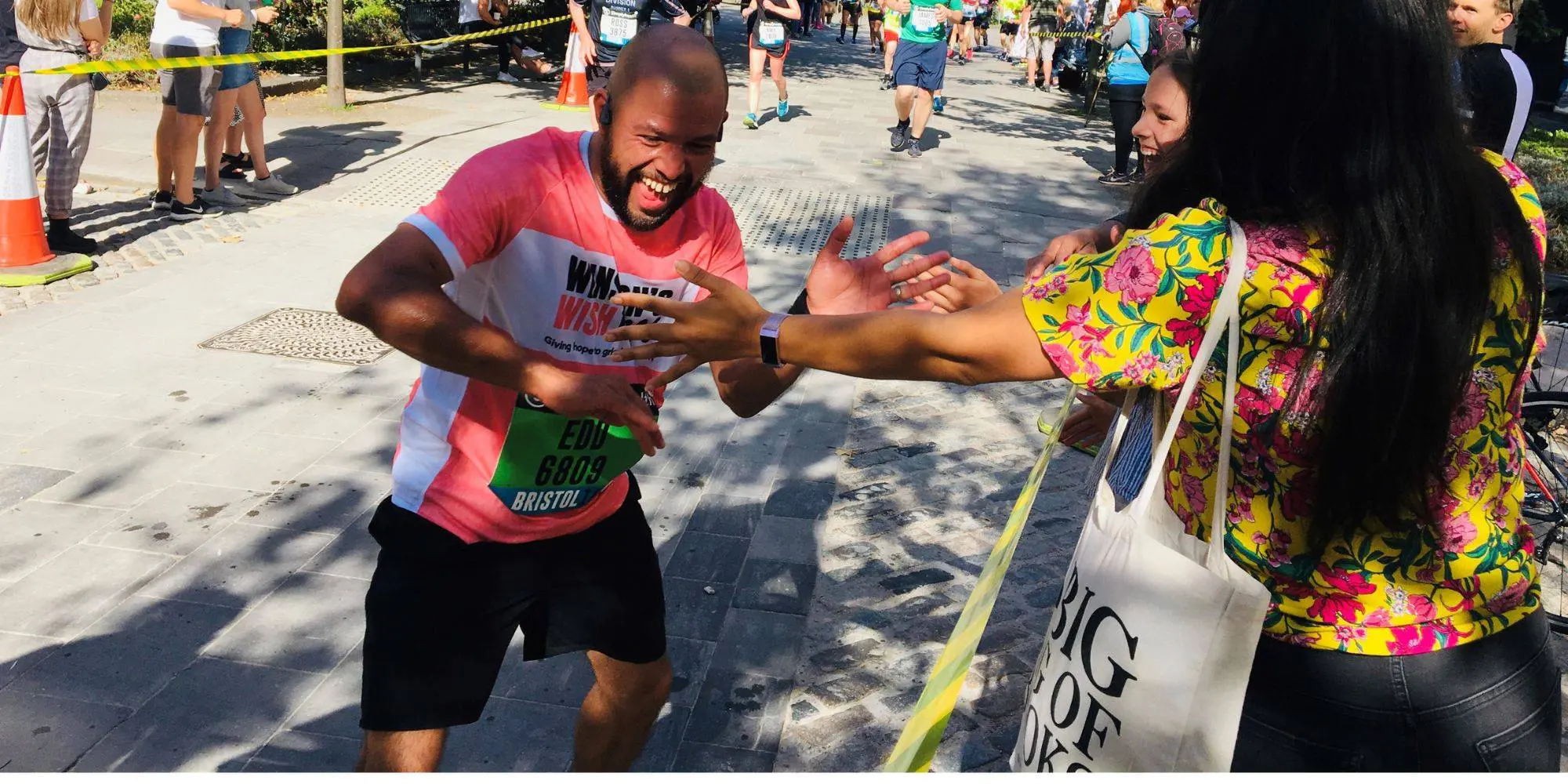 man getting high fives running past cherring crowd he is wearing a coral Winston's Wish running tshirt