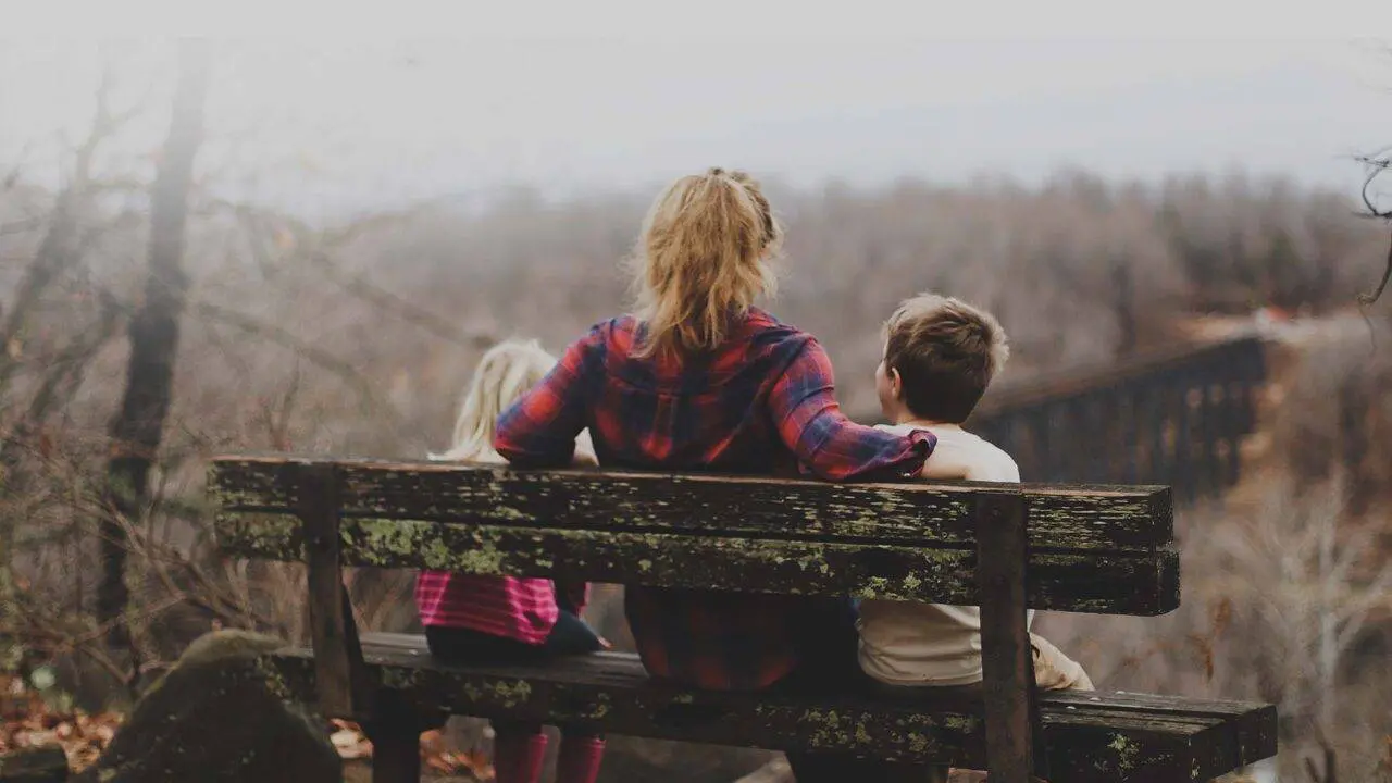 Mum and two young children sat on a bench looking at countryside - bereavement support services from Winston's Wish