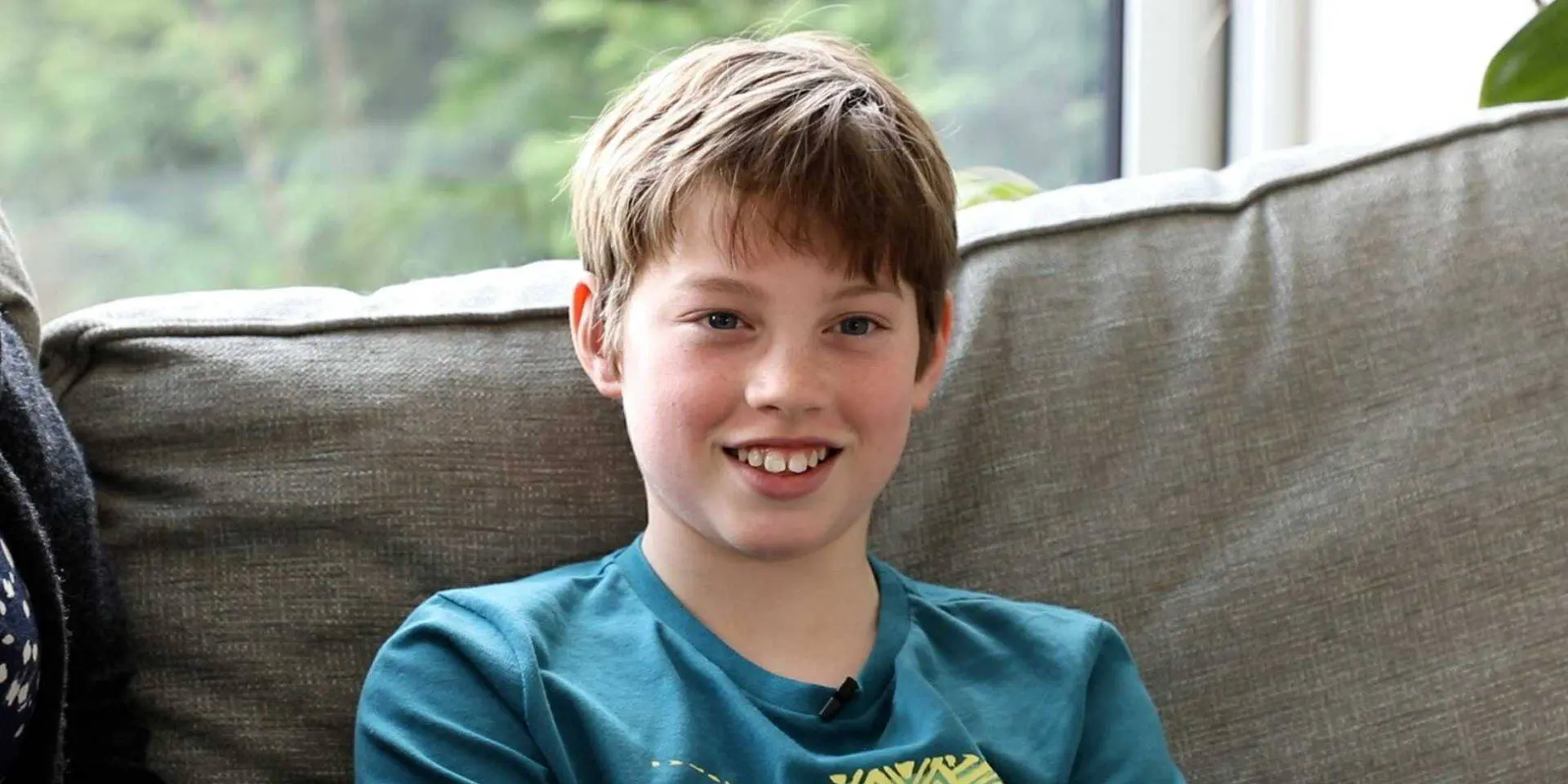 Photo of 11-year-old Harvey sat on a sofa, smiling at the camera
