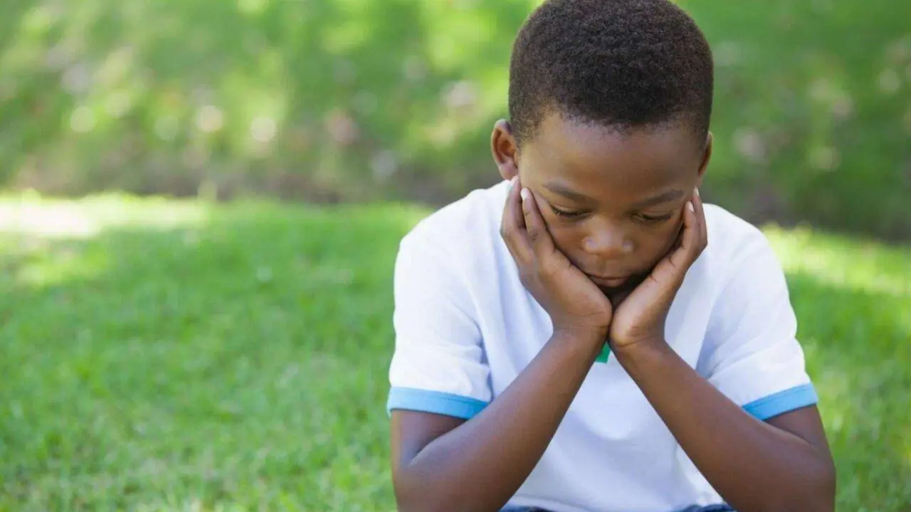 Young boy sitting on grass with his head resting in his hands