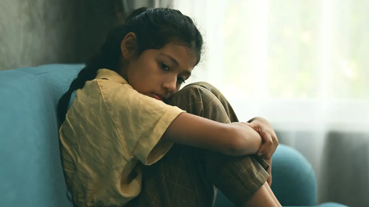 Young girl sat on the sofa, hugging her knees
