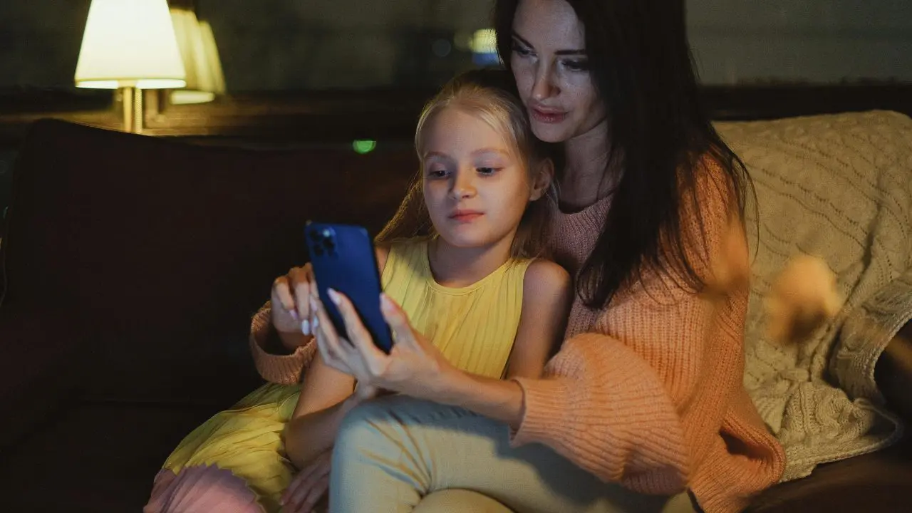 White mum using smartphone with daughter at home.
