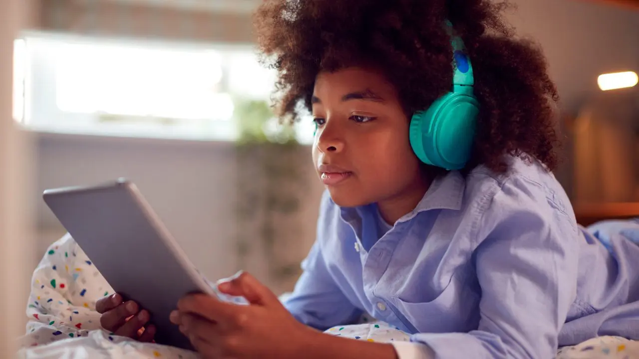 Black child wearing headphones looking at tablet device.