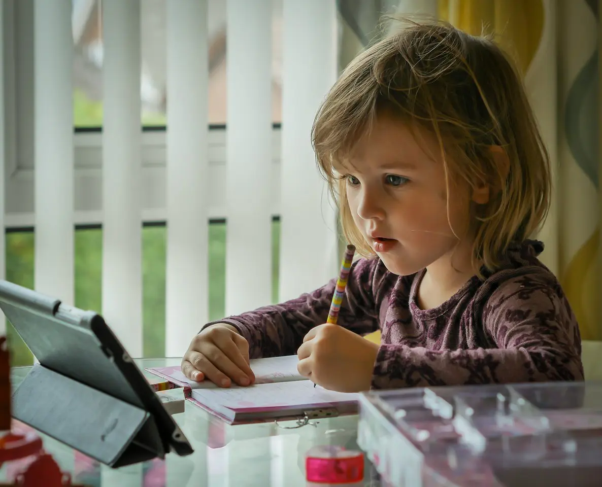 Child writing and looking at tablet device.