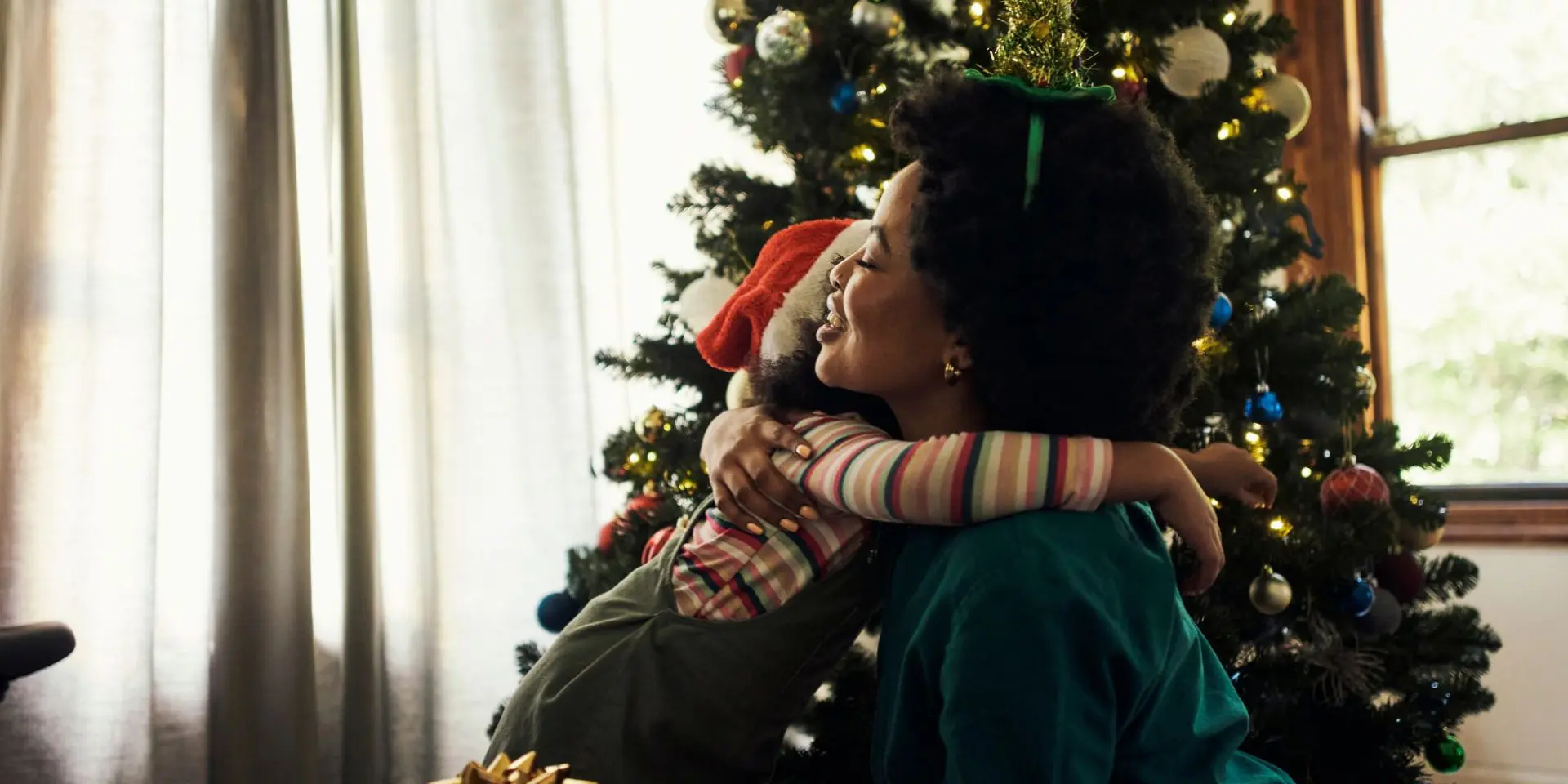 Woman hugging child in front of a Christmas tree - coping with grief at Christmas