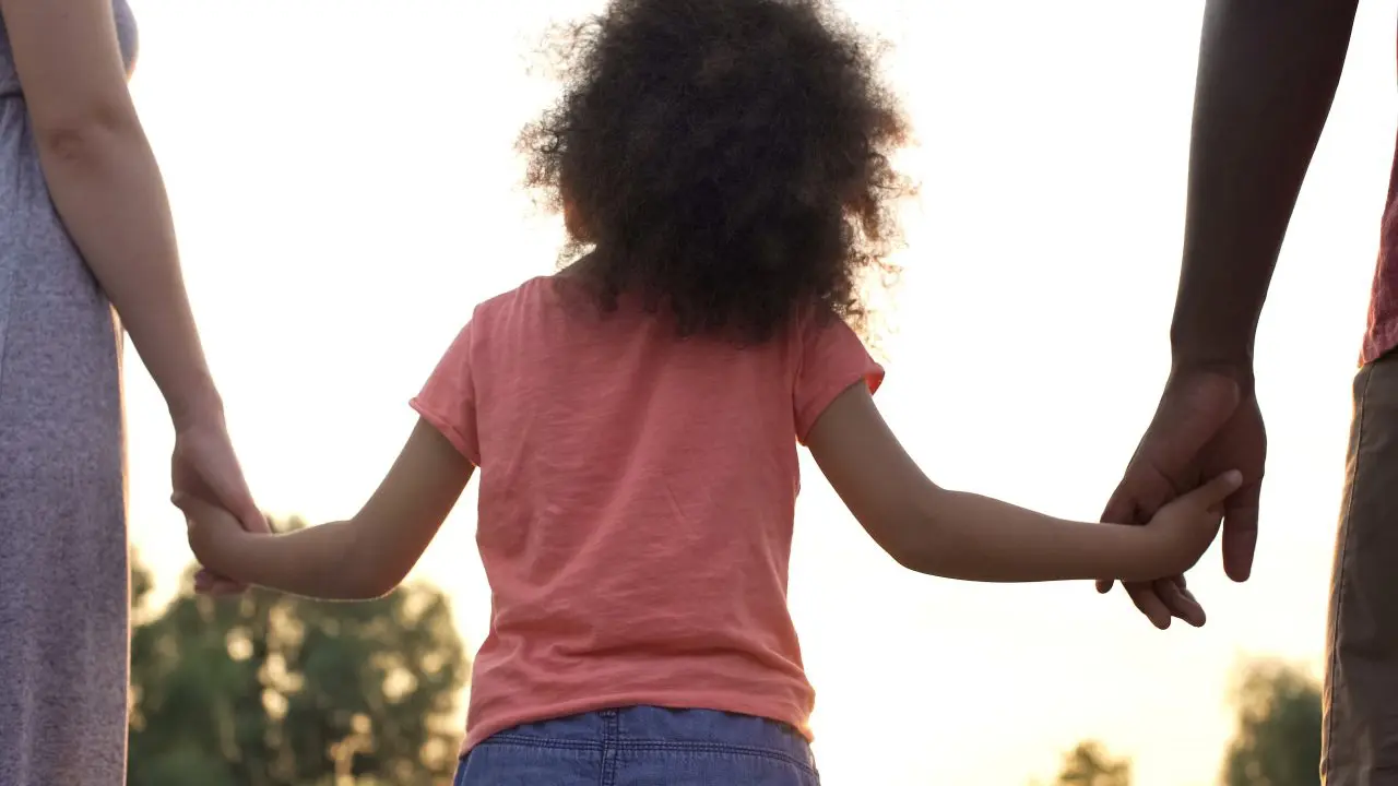 Child holding adult hands outdoors