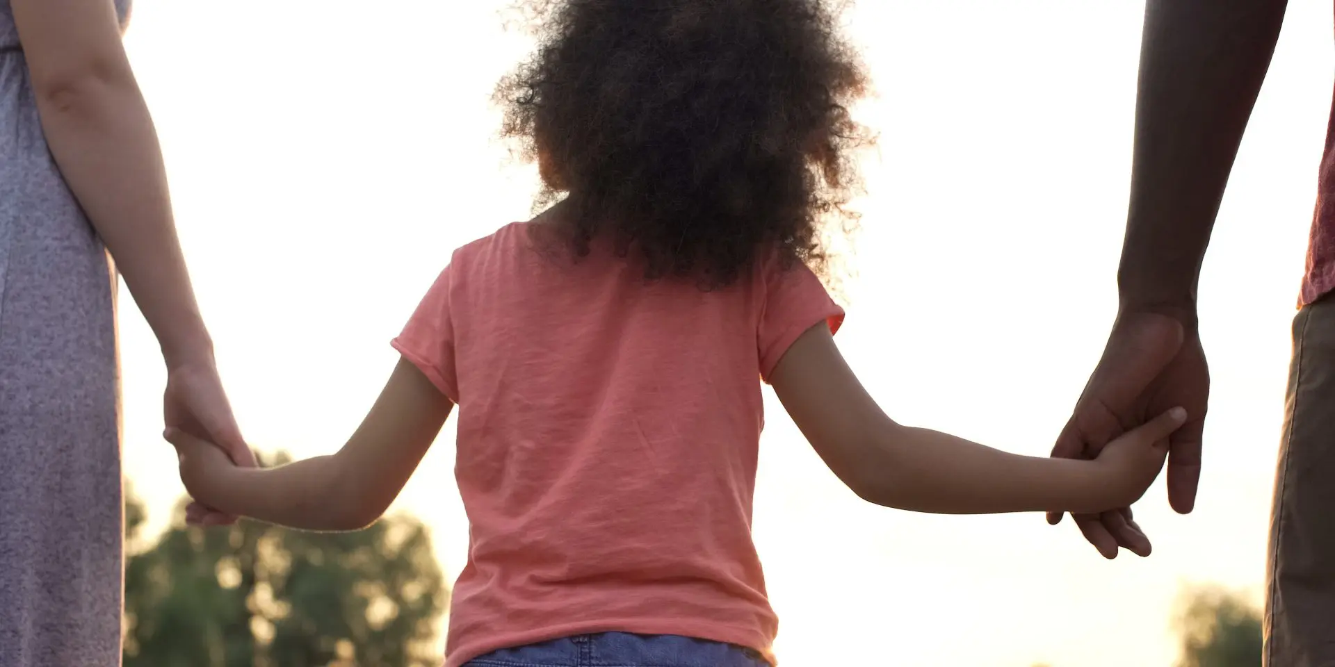Child holding adult hands outdoors