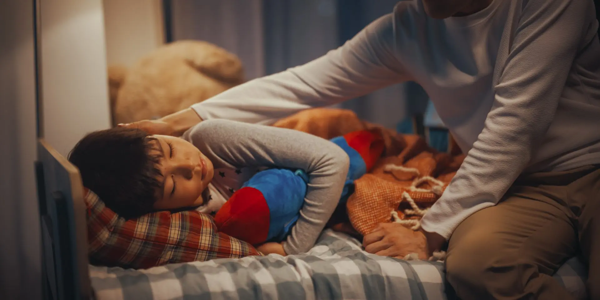 Young boy cuddling toy at bedtime and being comforted by parent