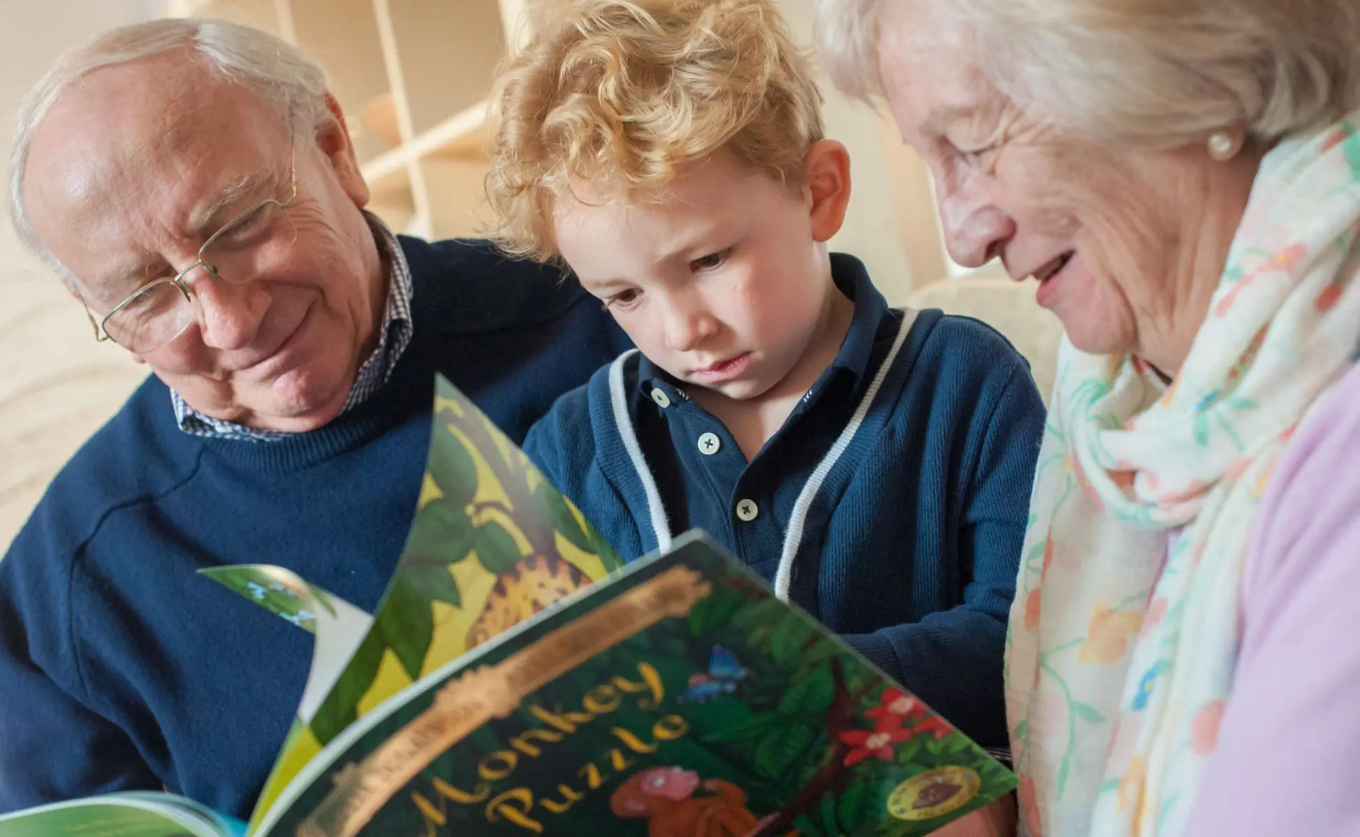 Young Child sat reading a picture book with his grandparents