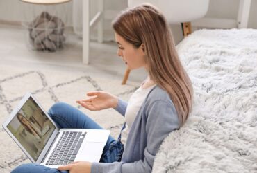Young woman sitting on the floor in a living room talking to a woman via video call on laptop