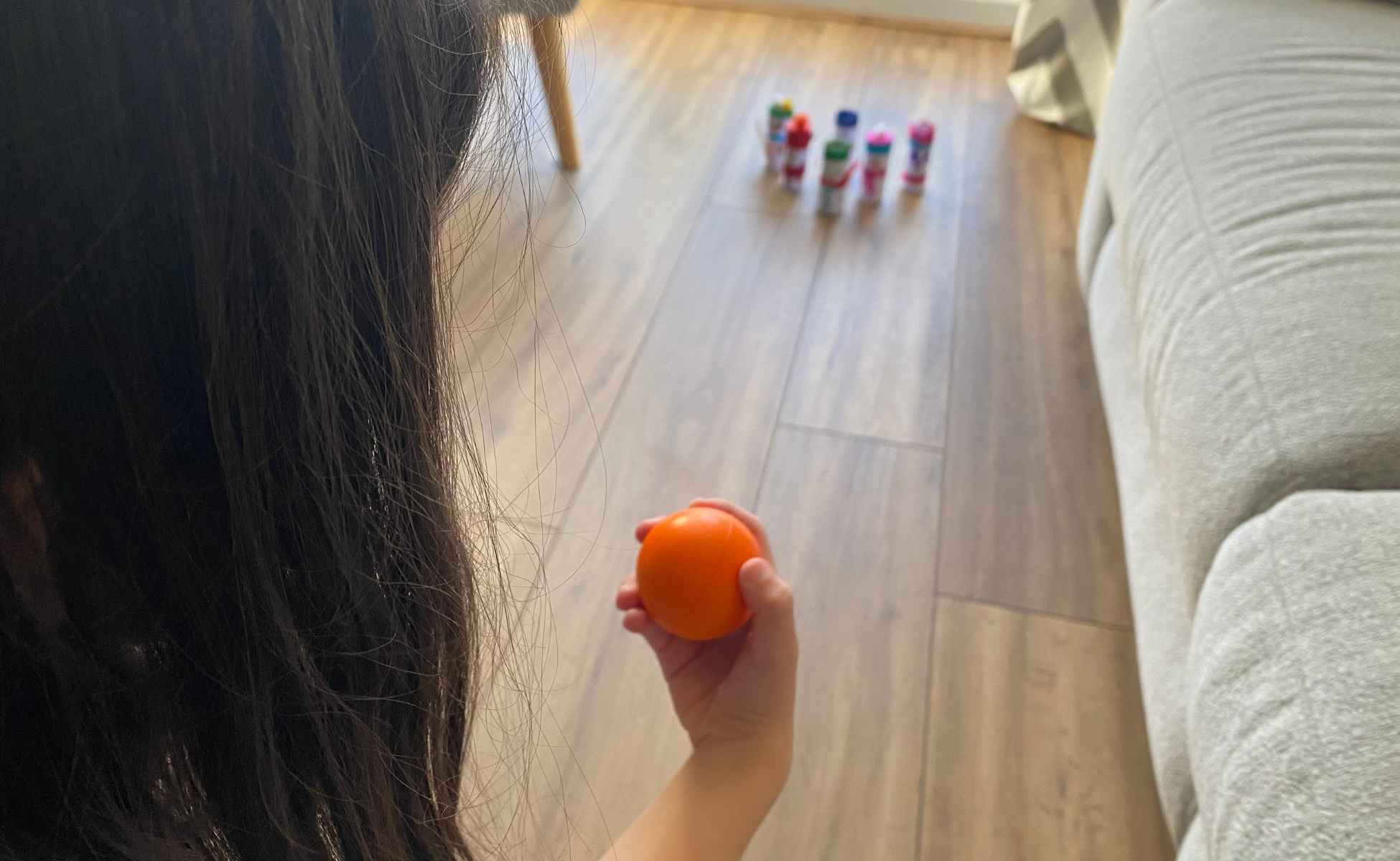 Snowmen lined up on the floor and a girl holding a ball ready to bowl it. Snowman strike Christmas activity step three.