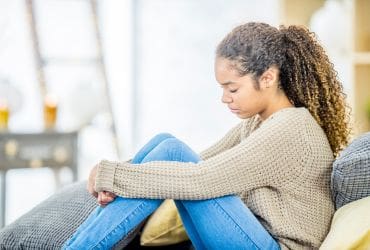 Young adult sat on sofa holding her knees